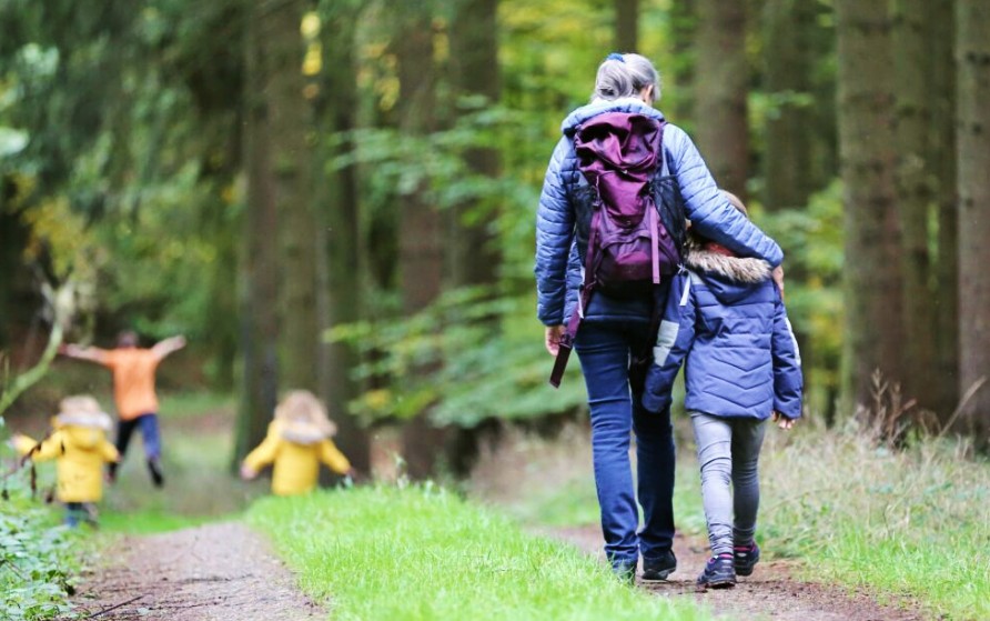 A woman and child walking in woods. The woman is hugging the child