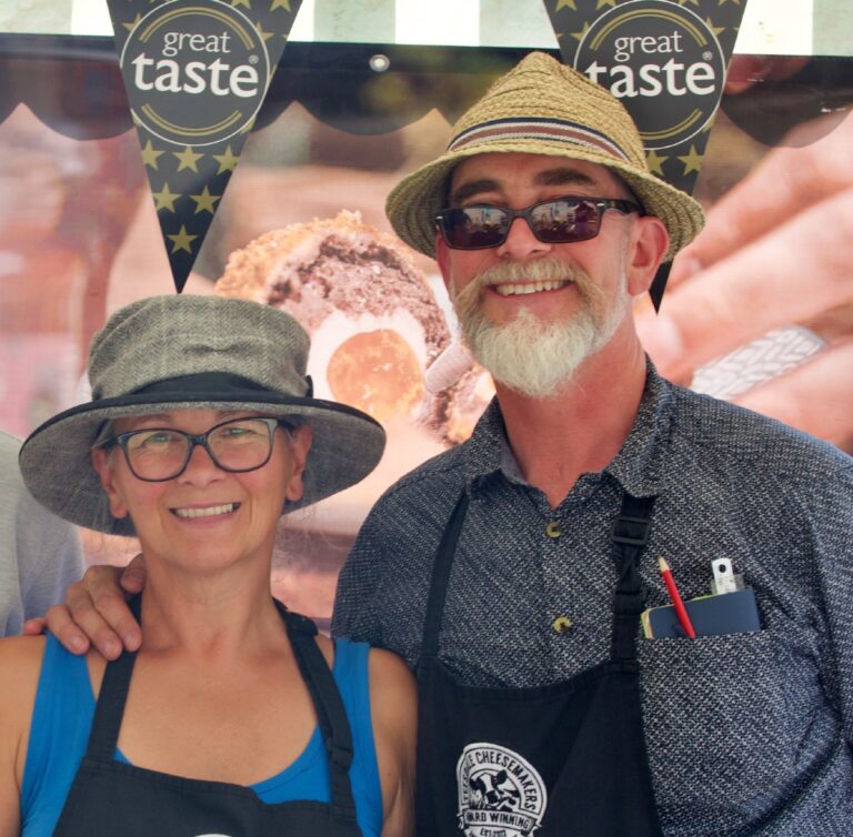 A man and woman, both farmers who make cheese. They are wearing hats