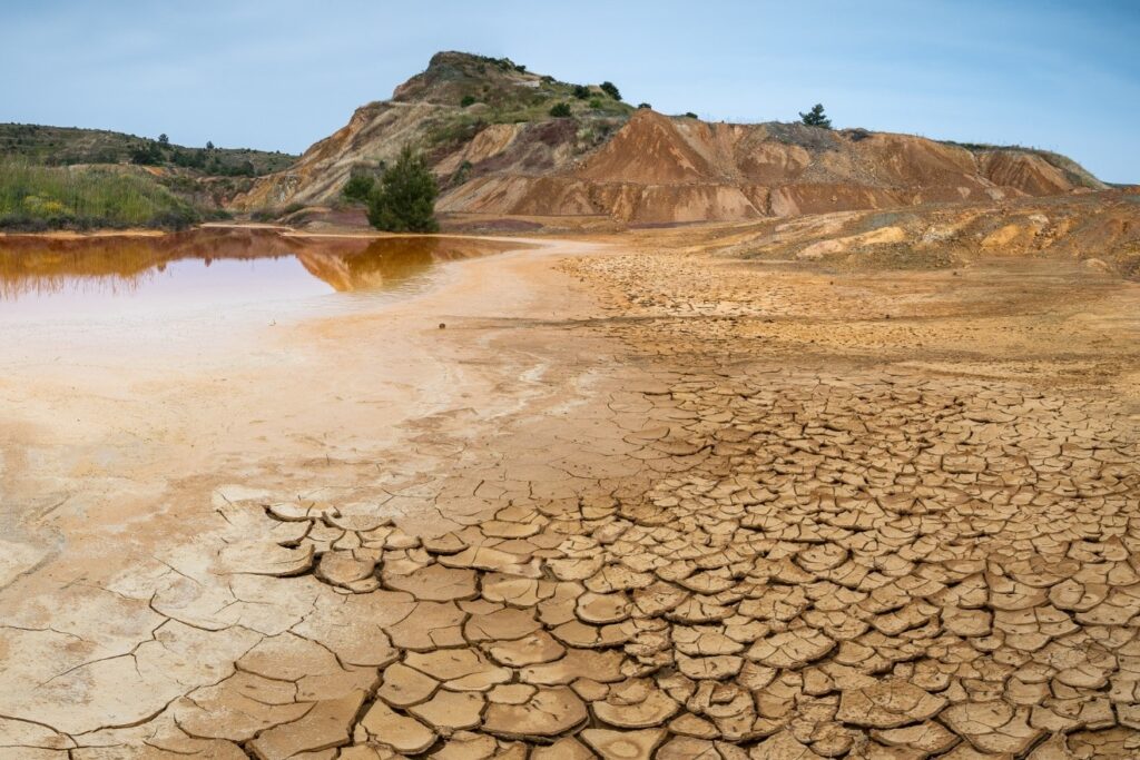 An expanse of cracked soil with an area of water that appears to be drying out