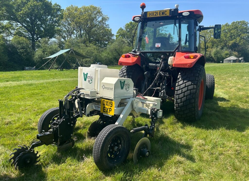 A red tractor in a field towing a mechanical device that helps soil