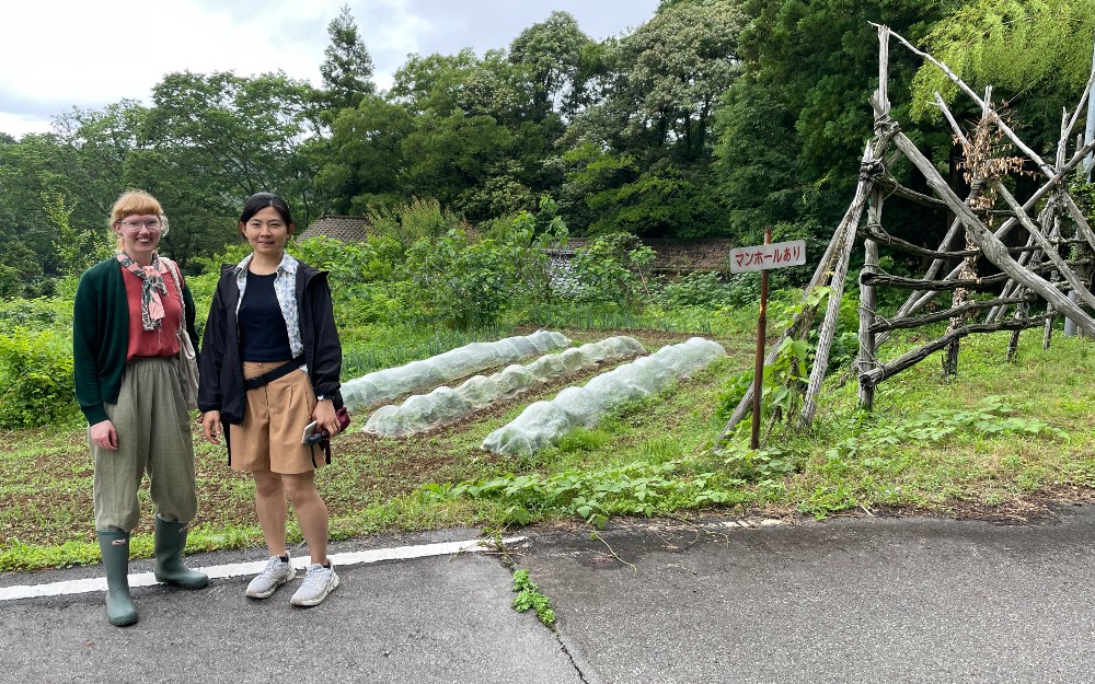 Two people stood in a rural area near a sign in japanese