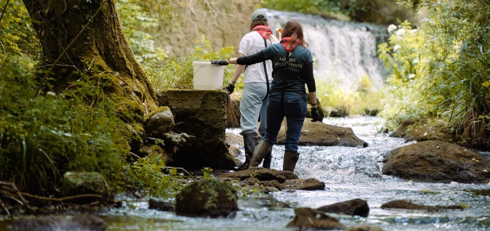 A river with two people wearing wellington boots standing in the river